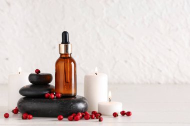 Doğal yağ şişesi, spa taşları, yanan mumlar ve hafif ahşap masa üzerinde dikenli dikenle kaplanmış bileşim.