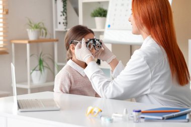 Female ophthalmologist putting trial frame on little girl in clinic