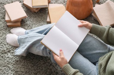 Evde halıda oturan boş bir kitabı olan kadın.