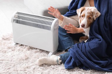 Battaniyeli genç kadın ve kaloriferin yanında ısıtan Avustralyalı çoban köpeği, yakın plan.