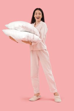 Pembe arka planda yastıkları olan güzel, mutlu bir kadın.