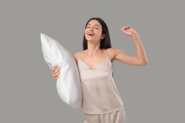 Gri arka planda yastığı olan güzel, mutlu bir kadın.