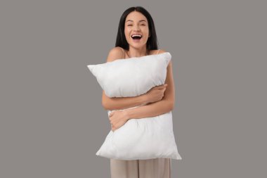 Gri arka planda yastığı olan güzel, mutlu bir kadın.