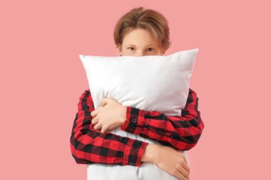 Pembe arka planda yastıklı, kareli pijamalı yakışıklı bir genç.