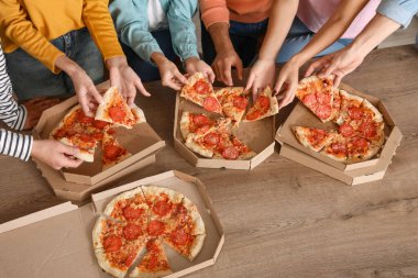 Bir grup arkadaş mutfaktaki masadan pepperonili pizza alıyor.