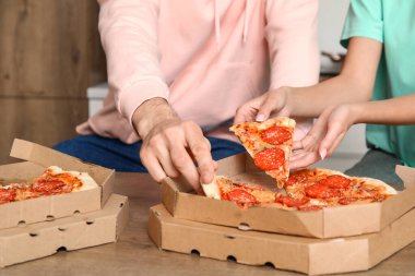 Genç çift mutfaktaki masadan pepperonili pizza alıyor, yakın plan.