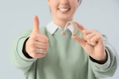 İşitme cihazı olan genç bir kadın arka planda baş parmak gösteriyor, yakın plan.