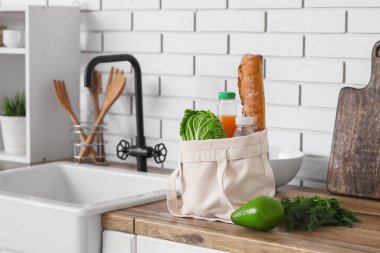 Mutfaktaki lavabonun yanında farklı taze ürünlerle dolu bir alışveriş çantası.