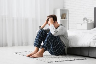 Yatak odasında halıda oturan depresif genç adam.