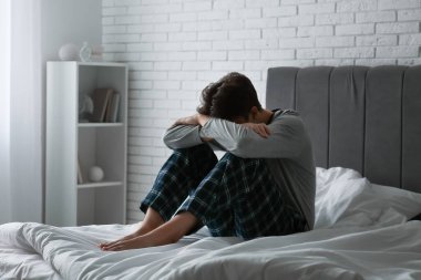 Depresyondaki genç adam karanlık yatak odasında oturuyor.