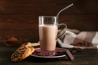 Bir bardak tatlı çikolatalı süt ve ahşap arka planda lezzetli kurabiyeler.