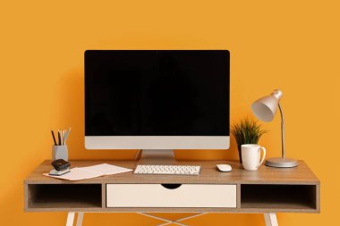 Sarı duvarın yanında bilgisayar ve kırtasiye malzemesi olan modern bir işyeri.