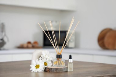 Mutfaktaki ahşap masa üzerinde kasımpatı çiçekleri ve gerekli yağla Reed dağıtıcı, yakın plan.