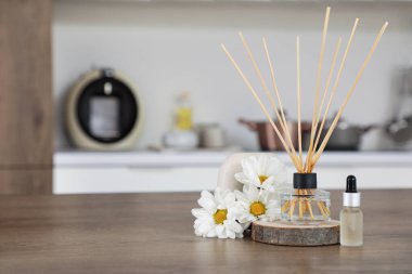 Mutfaktaki ahşap masa üzerinde kasımpatı çiçekleri ve gerekli yağla Reed dağıtıcı, yakın plan.