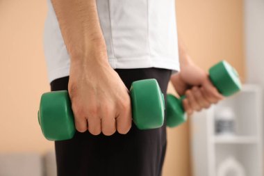 Sportif genç adam evde dambılları tutuyor, yakın plan.