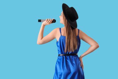 Mikrofonlu güzel bir kadın mavi arka planda karaoke söylüyor.