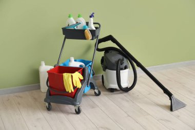 Yeşil duvarın yanında temizlik malzemeleri ve elektrikli süpürgeyle dolu bir araba.