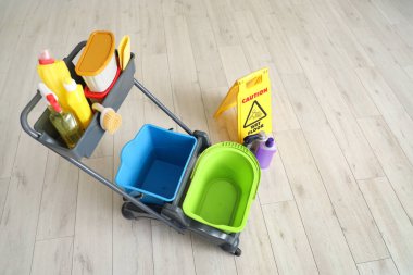 Evdeki ahşap zeminde temizlik malzemeleri ve uyarı levhası olan bir araba.