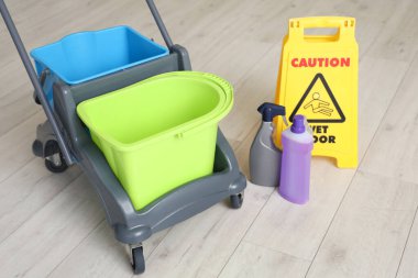 Evdeki ahşap zeminde temizlik malzemeleri ve uyarı levhası olan bir araba.