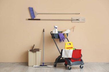 Temizlik malzemeleri, çöp tenekesi ve bej duvarın yanında uyarı levhası olan bir araba.