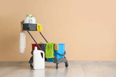 Bej duvarın yanındaki temizlik malzemelerinin olduğu vagon.