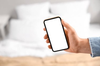 Yatak odasında boş cep telefonu tutan genç adam, yakın plan.