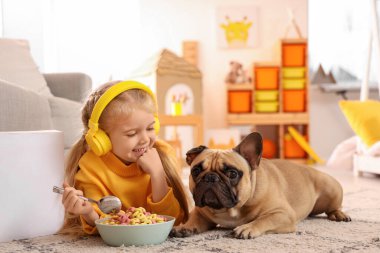 Evde lezzetli mısır gevreği halkaları yiyen kulaklıklı, sevimli, mutlu bir kız.