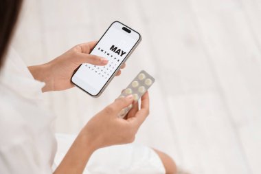 Östrojen hapları ve regl takvimi olan genç bir kadın banyoda cep telefonunda, yakın plan.