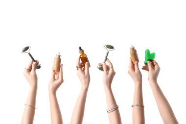 Kozmetik ürünleri şişeleri, yüz masajı aleti ve beyaz arka planda izole edilmiş Guasha ile birçok kadın eli.