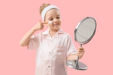 Pembe arka planda ayna kremi süren pijamalı tatlı küçük mutlu kız.