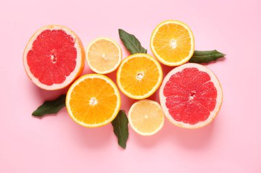 Pembe arka planda yaprakları olan farklı kesilmiş turunçgil meyveleri.