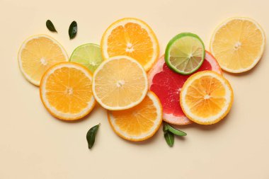 Bej arkaplanda farklı narenciye dilimleri ve yaprakları var.