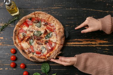 Kadın eli, siyah ahşap arka planda lezzetli bir pizza dilimi alıyor. Üst görünüm
