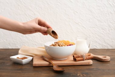 Lezzetli yulaf ezmesine tarçın ve ahşap masada, beyaz duvarın yanında böğürtlen ekleyen bir kadın eli.