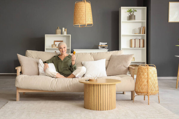 Зрелая женщина после химиотерапии с бутылкой травы, сидящей дома на диване