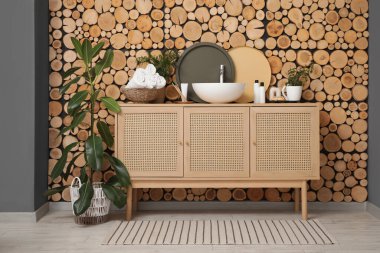 Ev bitkileri ve hasır sepet modern lavabonun üzerinde havlular banyodaki ahşap koçanlar duvarının yanında.