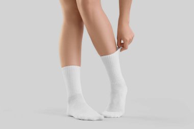 Gri arka planda şık beyaz çoraplar giyen genç bir kadın.
