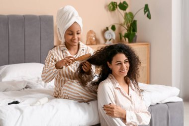 Mutlu Afro-Amerikalı kız annesinin kıvırcık saçlarını yatak odasında tarıyor.
