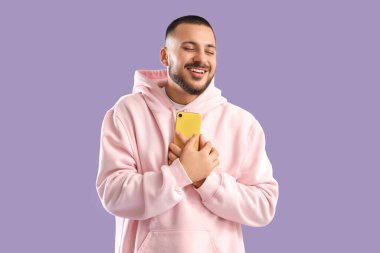 Leylak arka planında akıllı telefonu olan mutlu genç bir adam. Online randevu