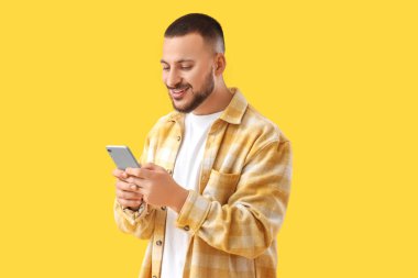 Cep telefonlu genç adam sarı arka planda sohbet ediyor.