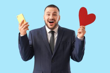 Mavi arka planda kalbi ve telefonu olan mutlu genç bir adam. Online randevu