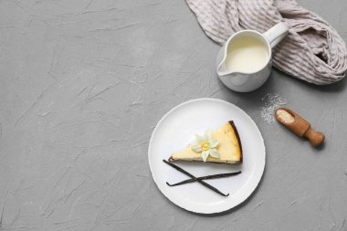 Bir parça tatlı vanilyalı cheesecake ve gri arka planda bir sürahi süt.
