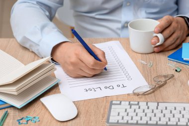 Yapılacaklar listesine sahip erkek eller ve ofisteki ahşap masada bir fincan kahve.