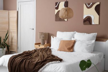 Konforlu yatak, yatak odasının içinde lamba ve katlanır ekran olan komodin.