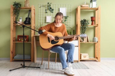 Stüdyoda mikrofonlu genç bir kadın gitar çalıyor.