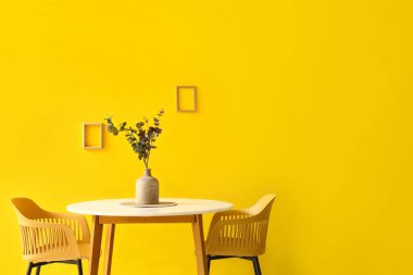 Okaliptüs dallı vazo yemek masasının üstünde, sarı duvarın yanında.
