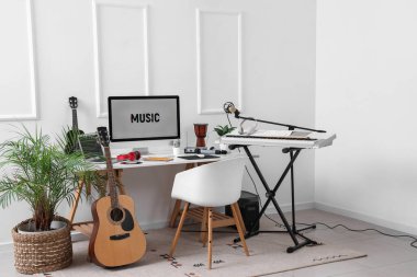 Stüdyoda ışık duvarı yakınında bilgisayar ve müzik aletleri olan bir işyeri