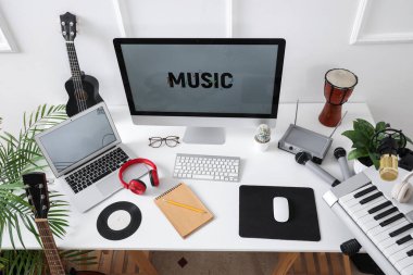Stüdyoda ışık duvarı yakınında bilgisayar ve müzik aletleri olan işyeri, üst görünüm