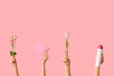 Pembe arka planda deterjan, paçavra ve çiçeklerle dolu kadın elleri.