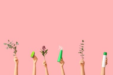 Pembe arka planda deterjan, sünger ve bitki dalları olan birçok kadın eli var.